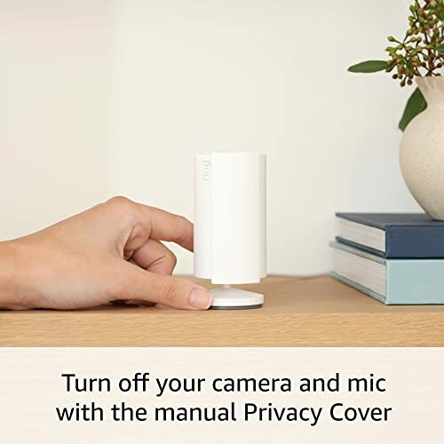 Person demonstrating a manual privacy cover on a white device with books and a vase in the background.